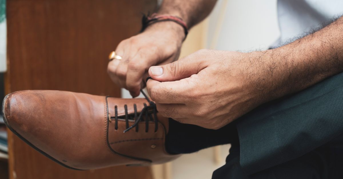 Detailed view of a man tying shoelaces on stylish brown leather shoes indoors.