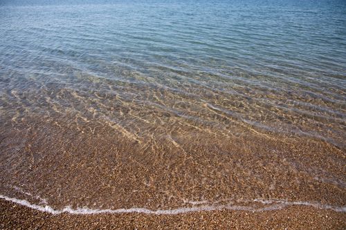 Free Serene beach with clear water and gentle waves, ideal for relaxation and tranquility. Stock Photo