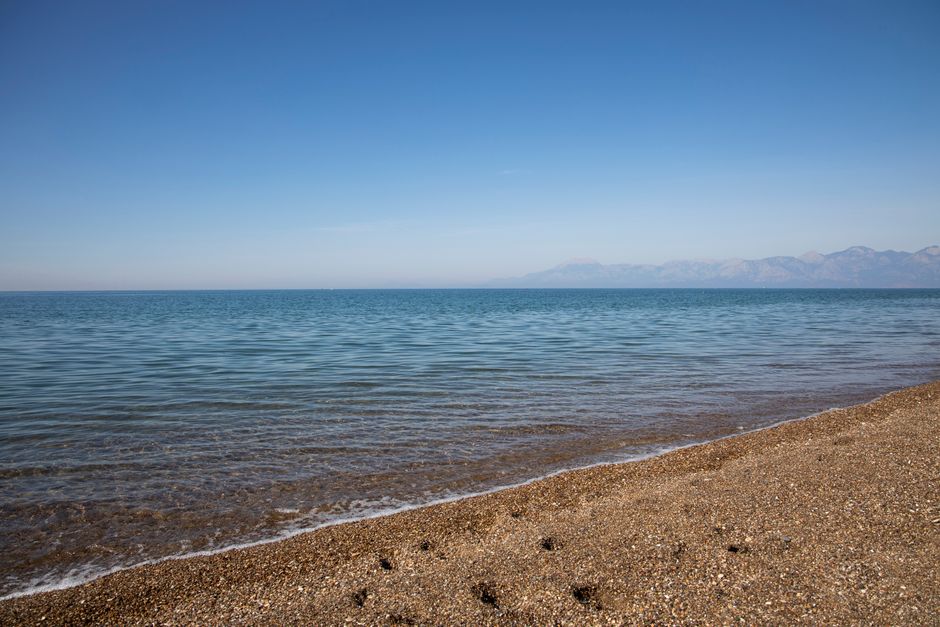 Peaceful seaside view of a clear ocean meeting the sandy beach under a bright blue sky.