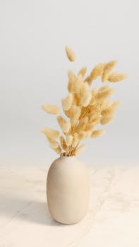 A simple, elegant composition featuring a minimalist ceramic vase with dried, fluffy flowers.