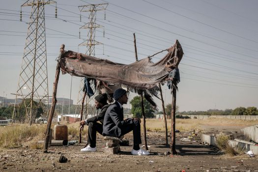 Full body side view of black male workers in elegant suits returned to native poor city and sitting in hut