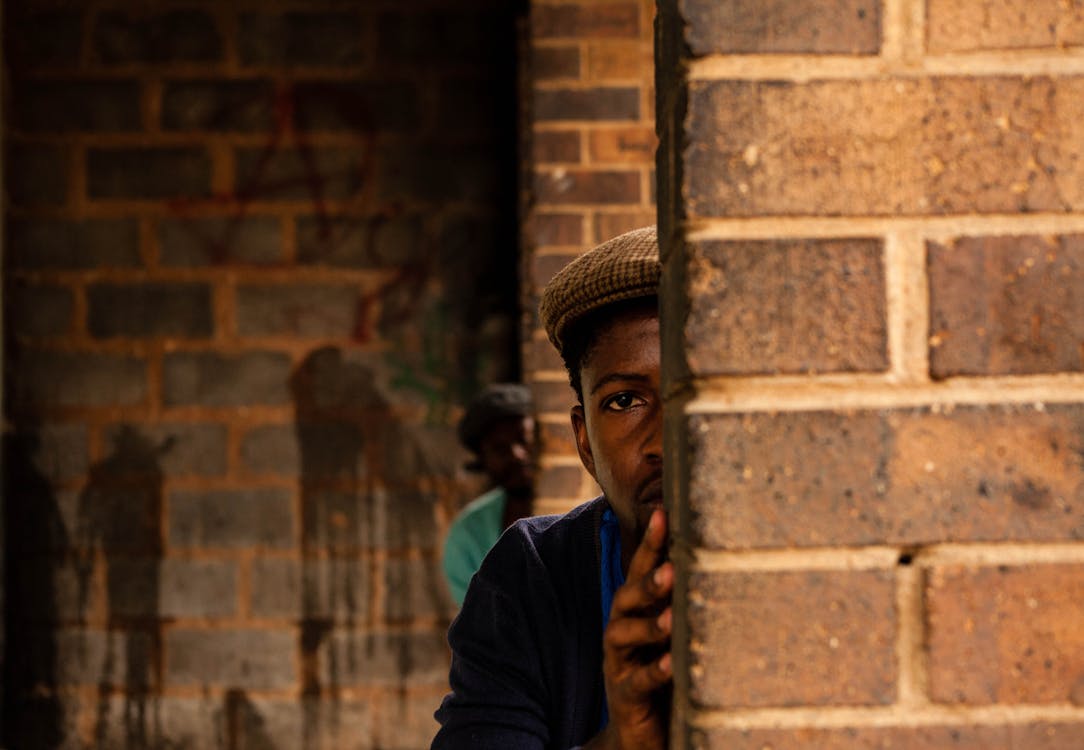 Free Serious African American males with frightened look hiding behind walls of brick building Stock Photo