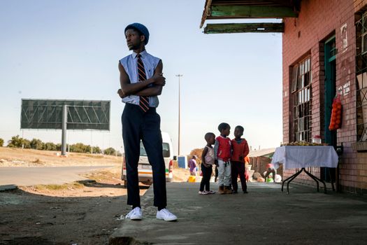 Stylish man contemplates on a street in Soweto, South Africa with children nearby.