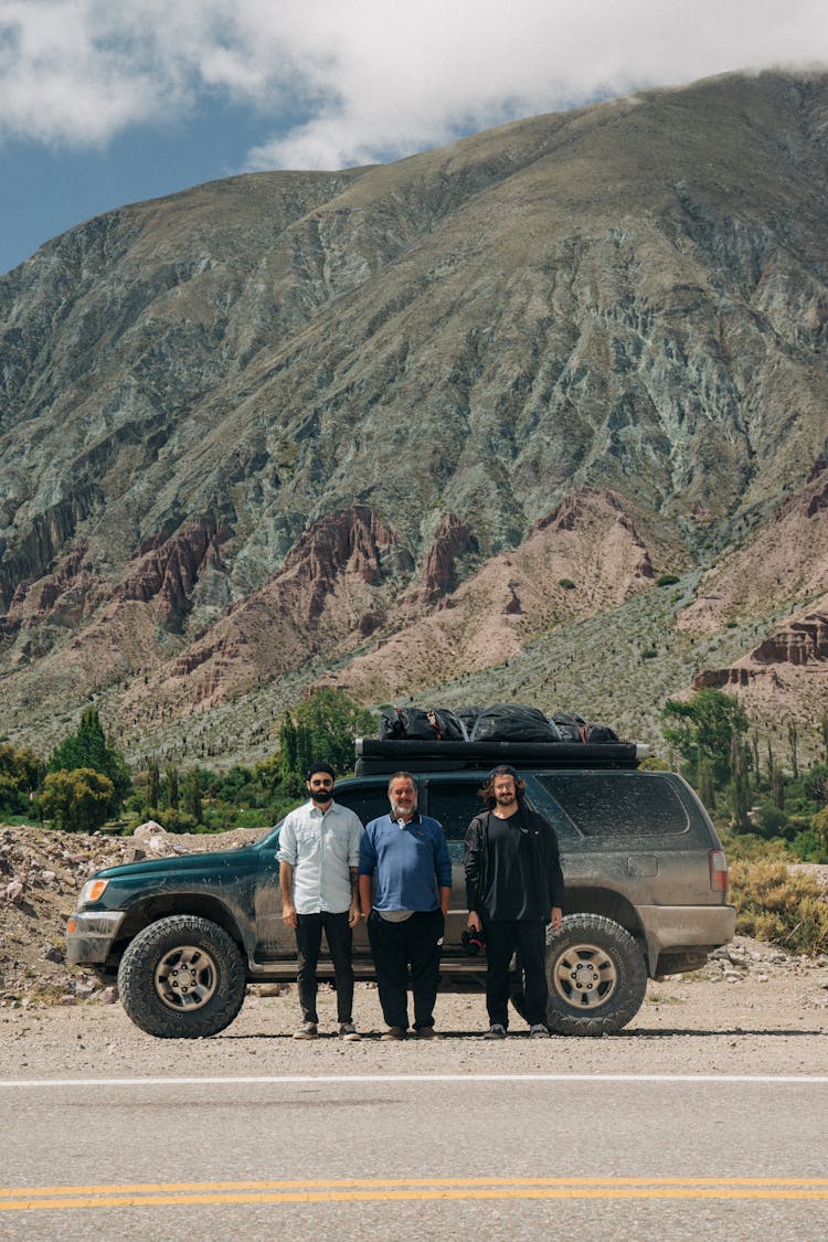 Group Of Men Standing In Row By Off-Road Car In Mountain Area