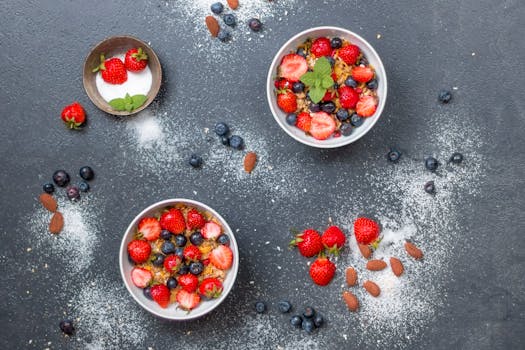 Top view of fresh berry and almond bowls with sugar on dark slate.