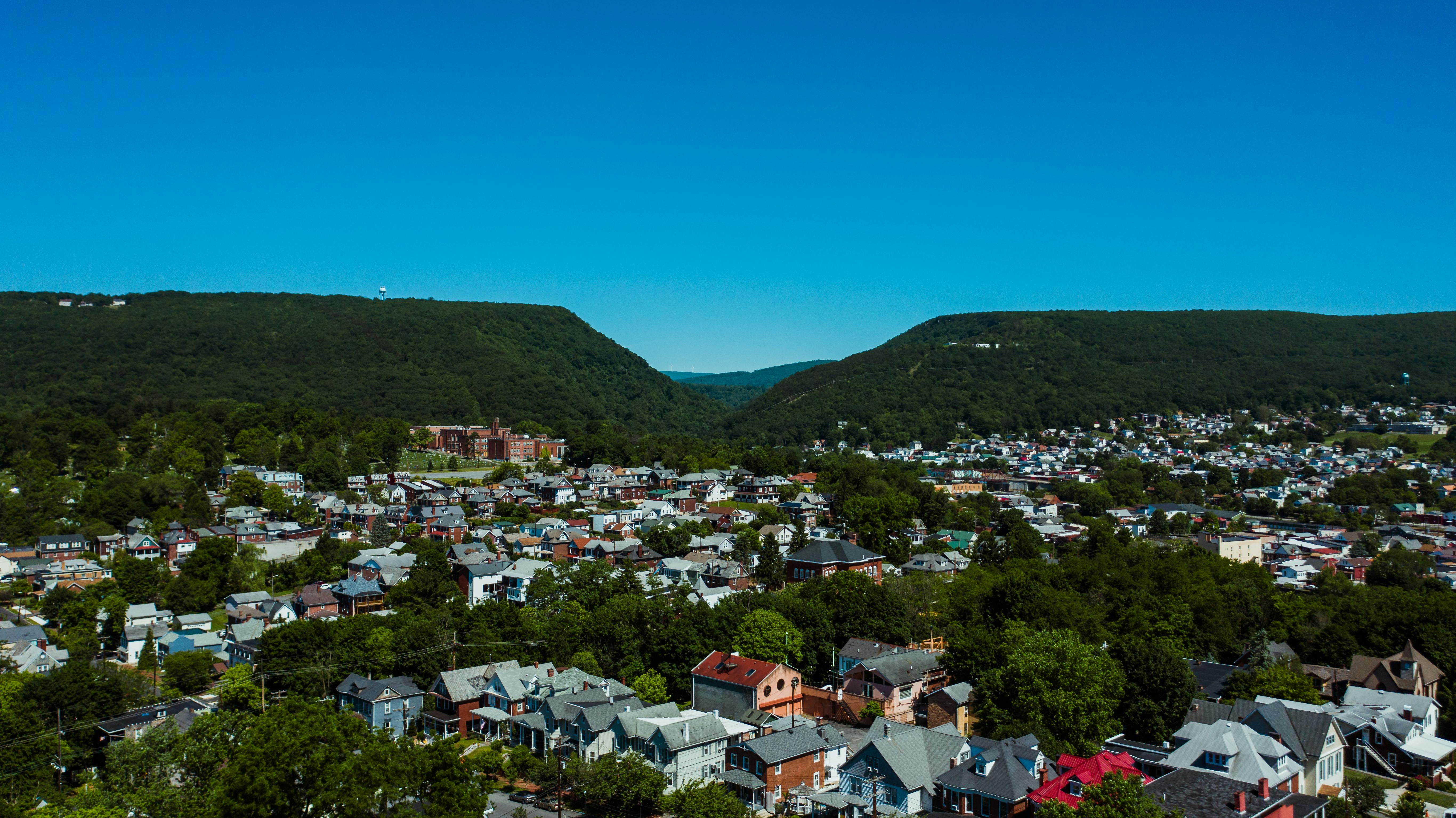 Aerial view of aged building exteriors near trees behind mounts under cloudless sky in daylight