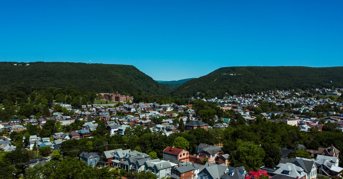 Aerial view of aged building exteriors near trees behind mounts under cloudless sky in daylight