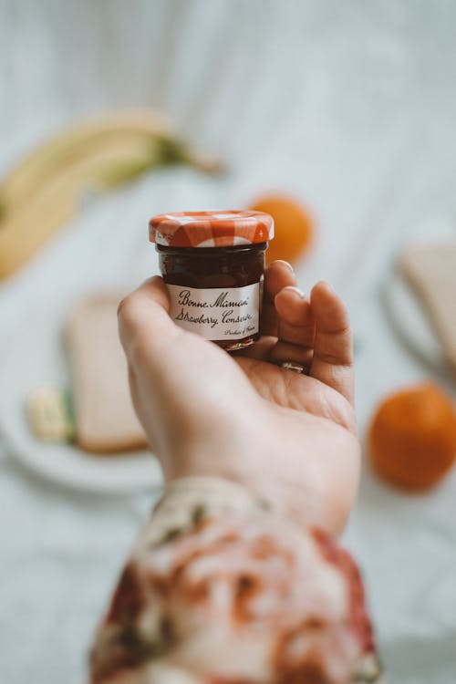 Crop unrecognizable person demonstrating small glass jar of homemade jam with written inscription