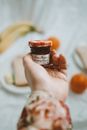 Crop unrecognizable person demonstrating small glass jar of homemade jam with written inscription