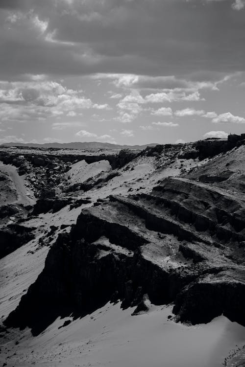 Grayscale Photo of Rocky Mountain Under Cloudy Sky