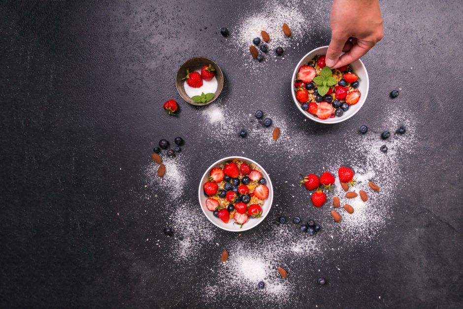 Fresh strawberries, blueberries, almonds in bowls on black table with hand arranging. - Price vs. Quality of Nuts: Making the Right Choice