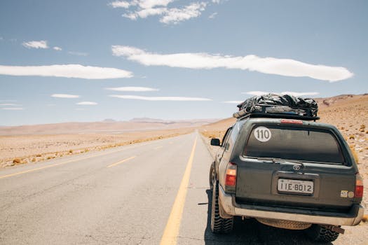 A rugged SUV travels along a remote desert highway in Jujuy, Argentina under a clear blue sky.