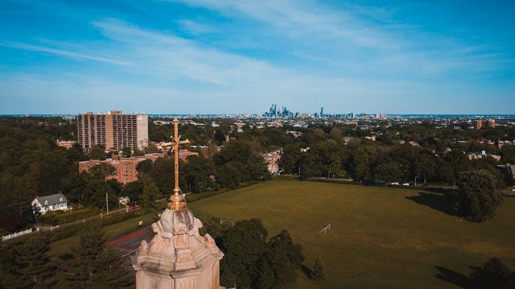 Golden Cross Of Old Temple Near Grass Lawn In Town