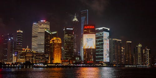 Contemporary multistage building exteriors with inscriptions near shiny rippled river in city at night