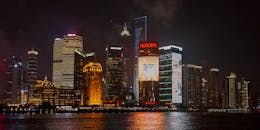 夜间，城市波光粼粼的河流附近，一栋刻有铭文的当代多层建筑外观