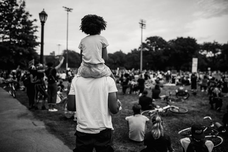 Person With A Child On His Shoulders Looking At A Protest