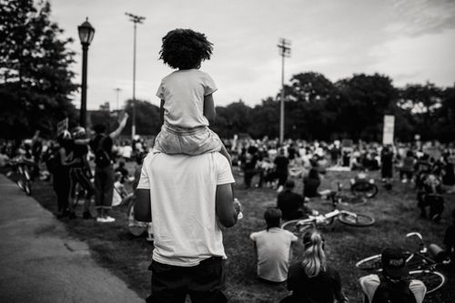 Free Grayscale image of a father with child on shoulders at a peaceful outdoor protest. Stock Photo
