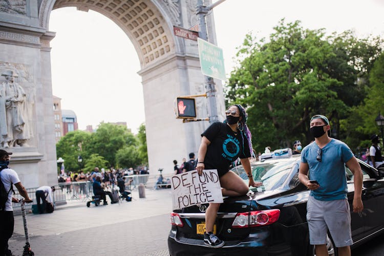 Woman Kneeling On The Back Of A Car And Holding A Sign