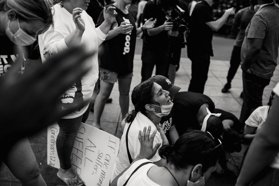 A crowd of diverse adults praying together at an outdoor protest, showcasing unity and solidarity.