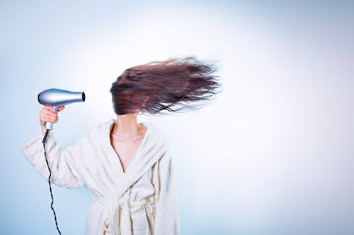 Woman Holding Gray Hair Dryer and Wearing White Bathrobe