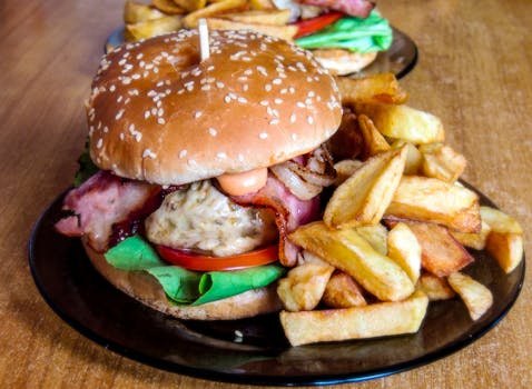 Close-up of a homemade burger with crispy bacon, lettuce, and fries on a plate.
