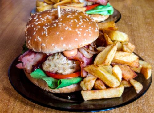 Free Close-up of a homemade burger with crispy bacon, lettuce, and fries on a plate. Stock Photo