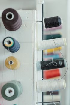 Close-up of various colored spools of thread organized on a sewing rack indoors.