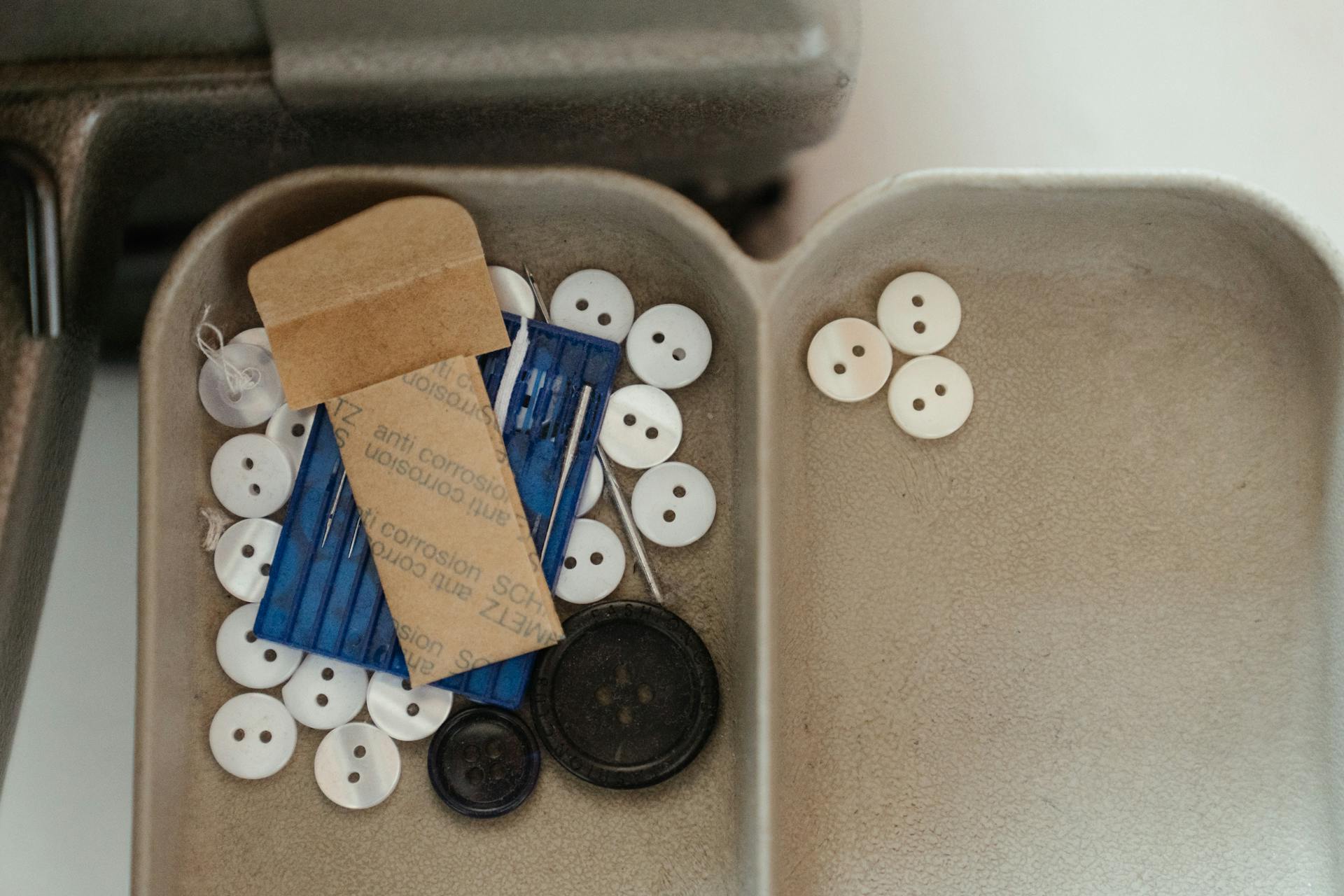 Close-up of a sewing tray with various buttons and needles, ideal for crafting themes.