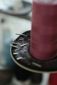Detailed view of a pink thread spool surrounded by sewing needles, in a workshop setting.