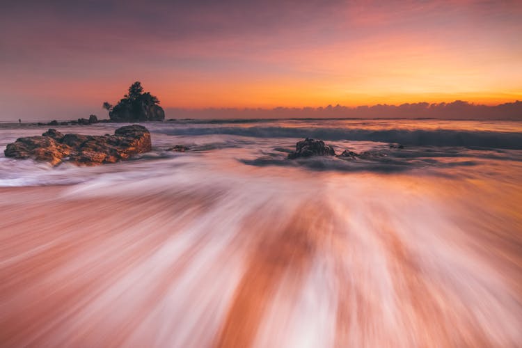 Stormy Sea With Fast Water Flow On Beach At Sunset