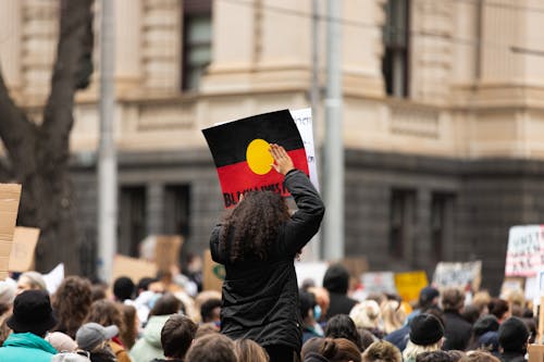 Curly Haired Person Wearing Black Jacket Holding a Poster with Message 