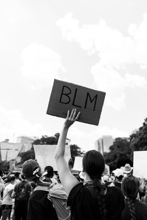 Grayscale Photo of a Protester Holding a Cardboard Sign