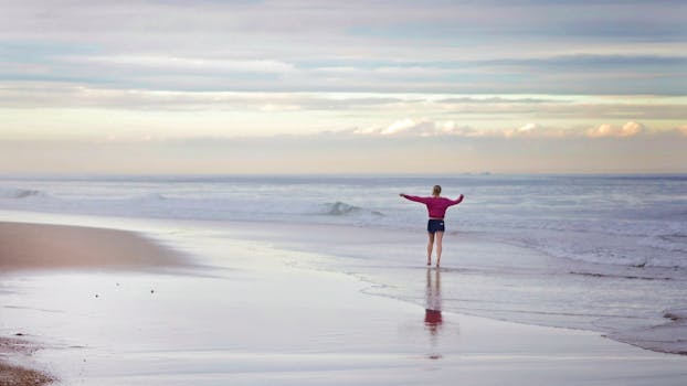 A woman stands at the edge of the ocean embracing serenity on the beach.
