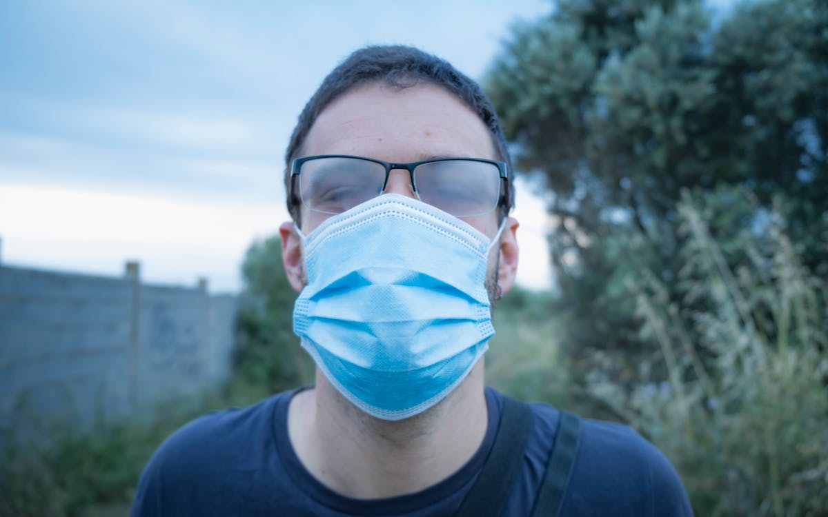 Close-up of a man wearing a face mask and eyeglasses with foggy lenses in an outdoor setting.