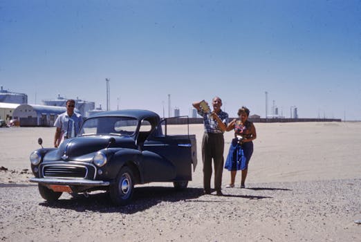 Two men and a woman standing by a vintage car in a desert landscape.