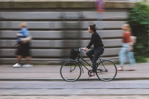 Free Side view of male in casual wear riding bike with basket on roadway near pavement in town Stock Photo