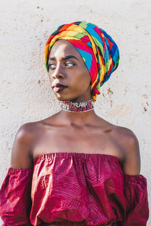 Dreamy black woman in bright headscarf near rough wall