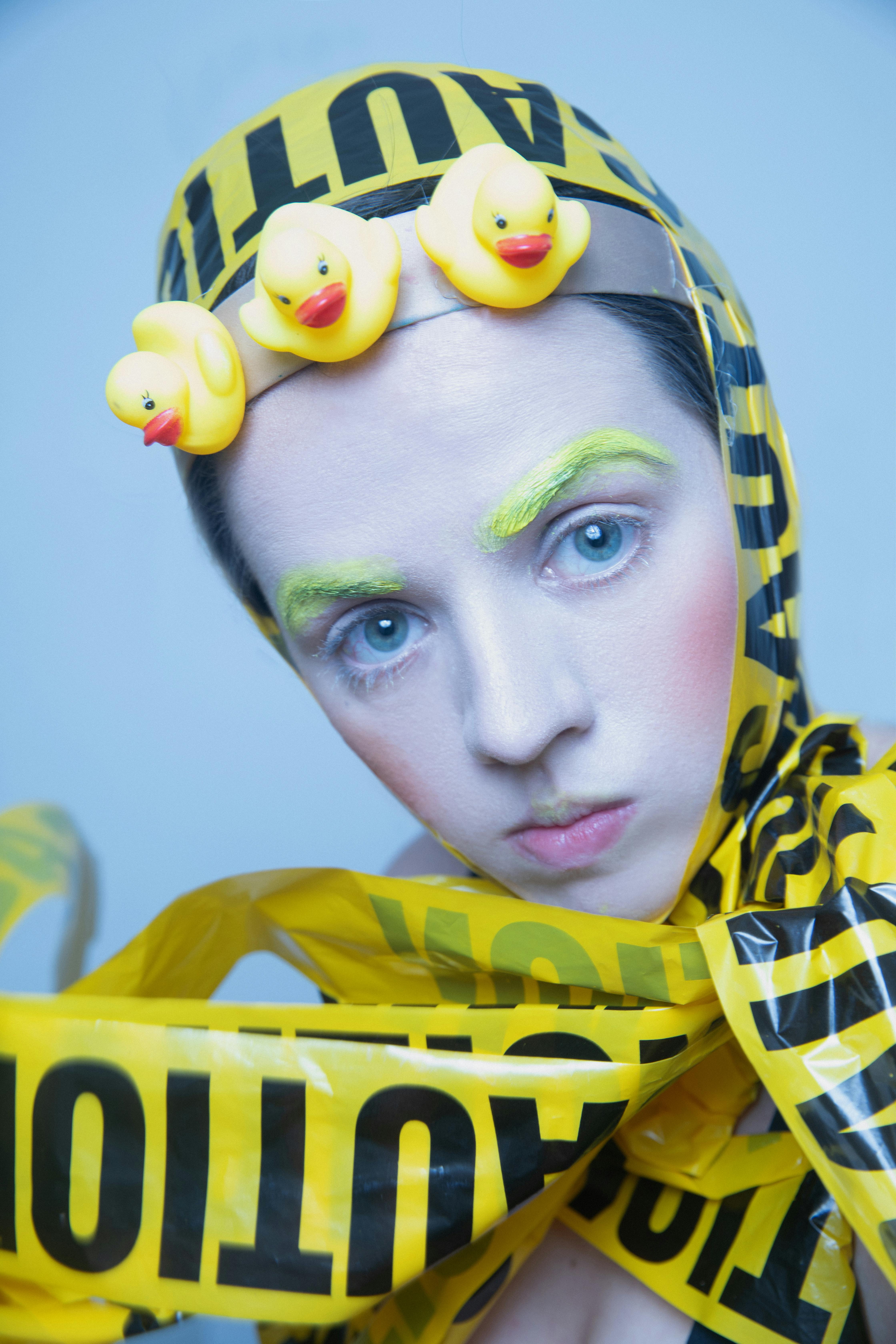 A unique artistic portrait of a woman wrapped in caution tape with rubber ducks on her head.