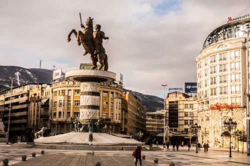 Free Aged stone sculpture of warrior on horse near house facades and snowy mountain under cloudy sky in town Stock Photo