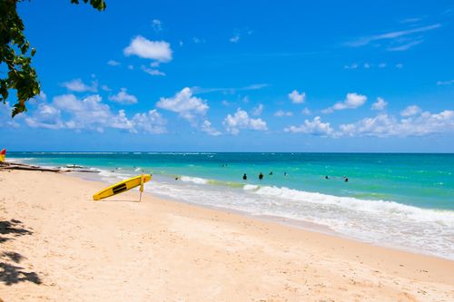 Free Idyllic tropical beach with turquoise waters, sandy shore, and a yellow surfboard under a bright blue sky. Stock Photo