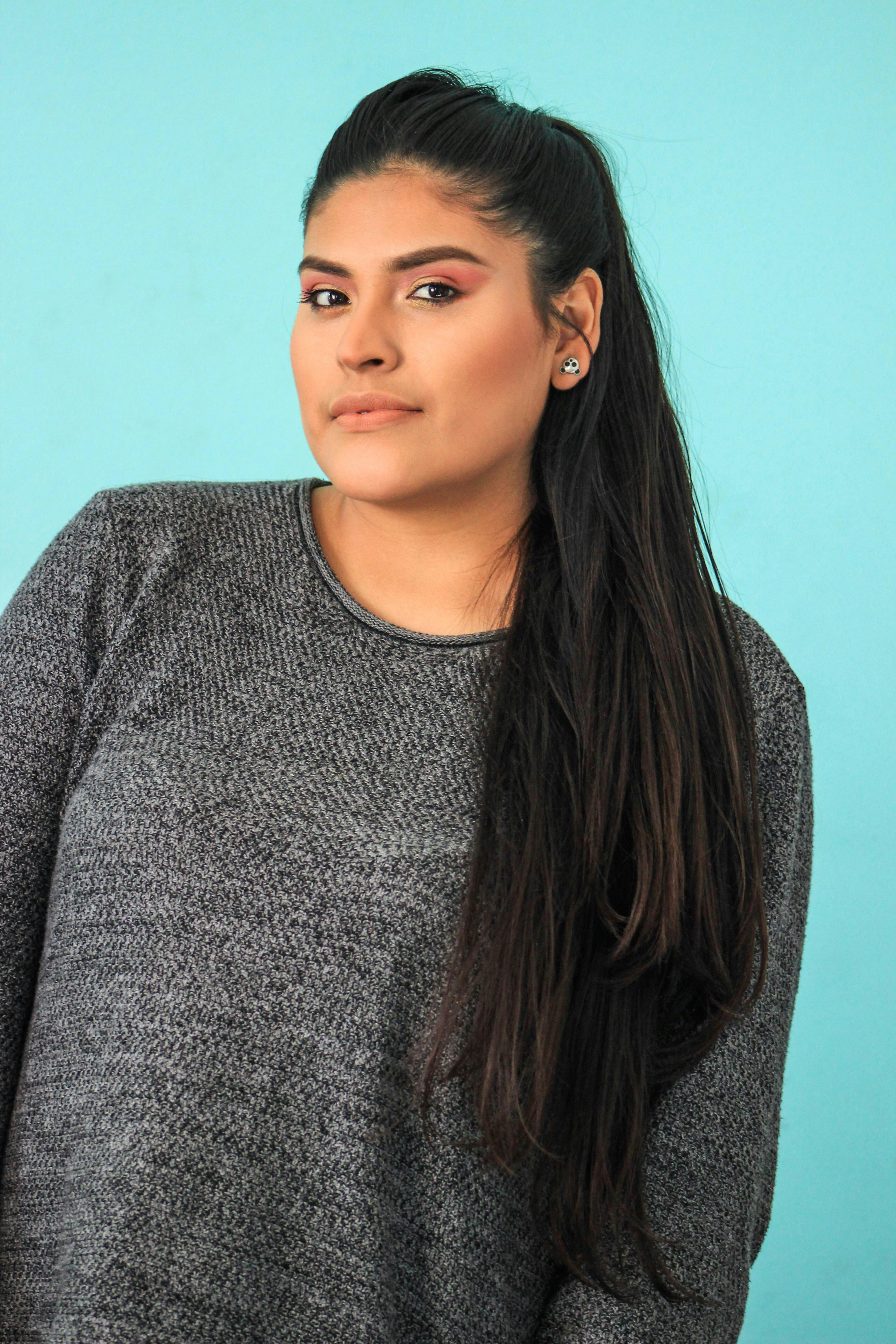 Studio portrait of a woman wearing a knitted sweater against a light blue backdrop.