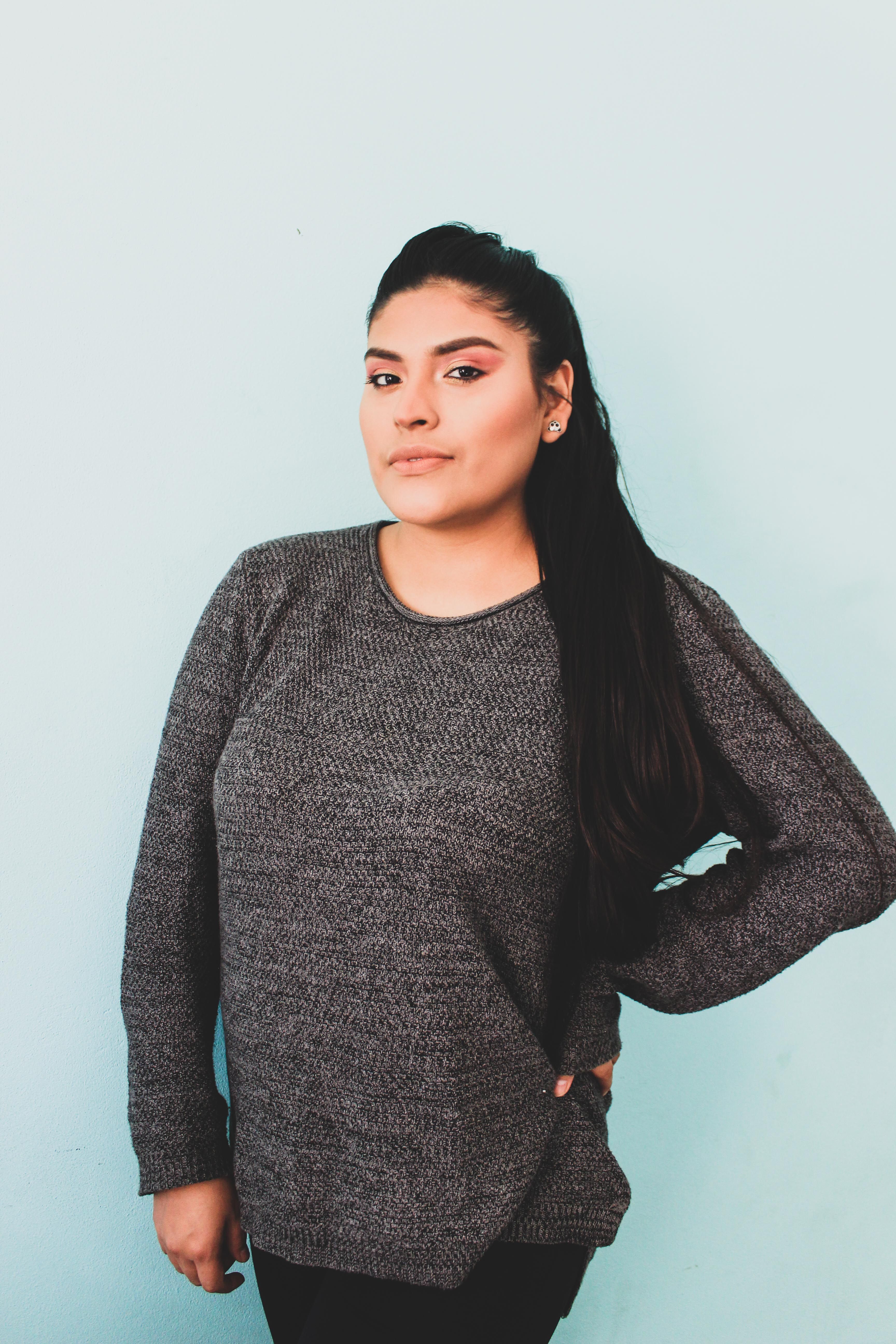 Portrait of a confident woman posing with hand on hip against a light blue background, showcasing casual fashion.