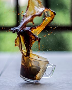 Coffee splash captured in motion as it spills from a tilting glass mug, creating a dynamic and artistic effect.