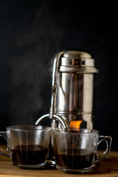 Metal coffee maker with glass cups on table