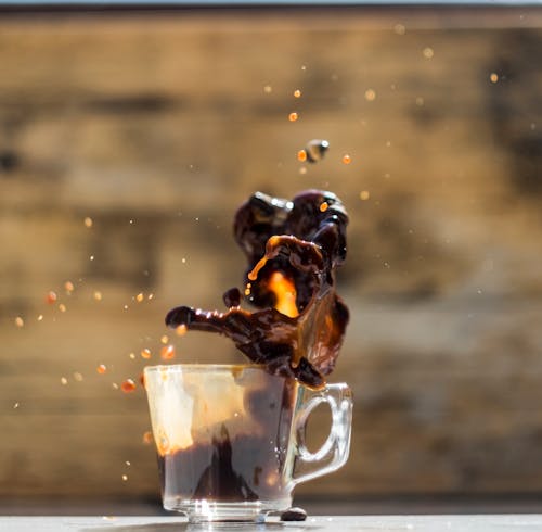 Transparent glass cup with fast coffee fluid with small drips above table in house