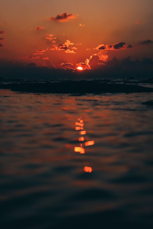 Dark sunset sky with clouds reflecting peacefully on rippling surface of sea water