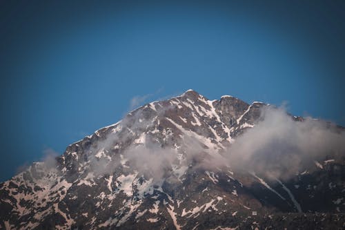 Severe scenery of rough rocky mountain with slopes covered with snow under cloudless blue sky