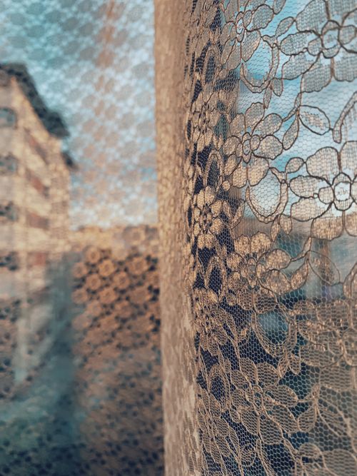 Free Closeup of white lace curtain with floral pattern on apartment window against modern residential complex buildings Stock Photo