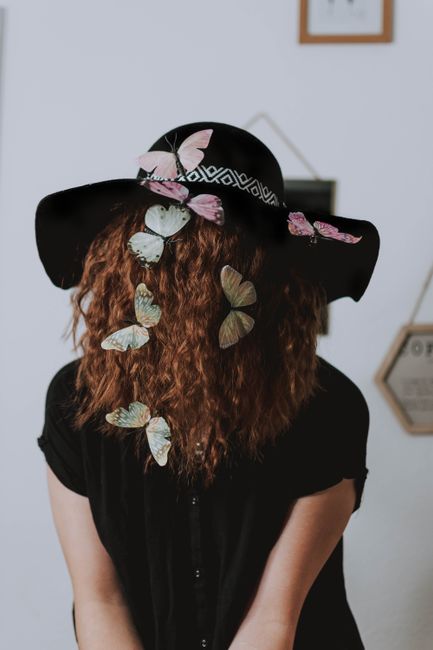 A woman wearing a hat adorned with butterflies and curly hair, creating a dreamy aesthetic.