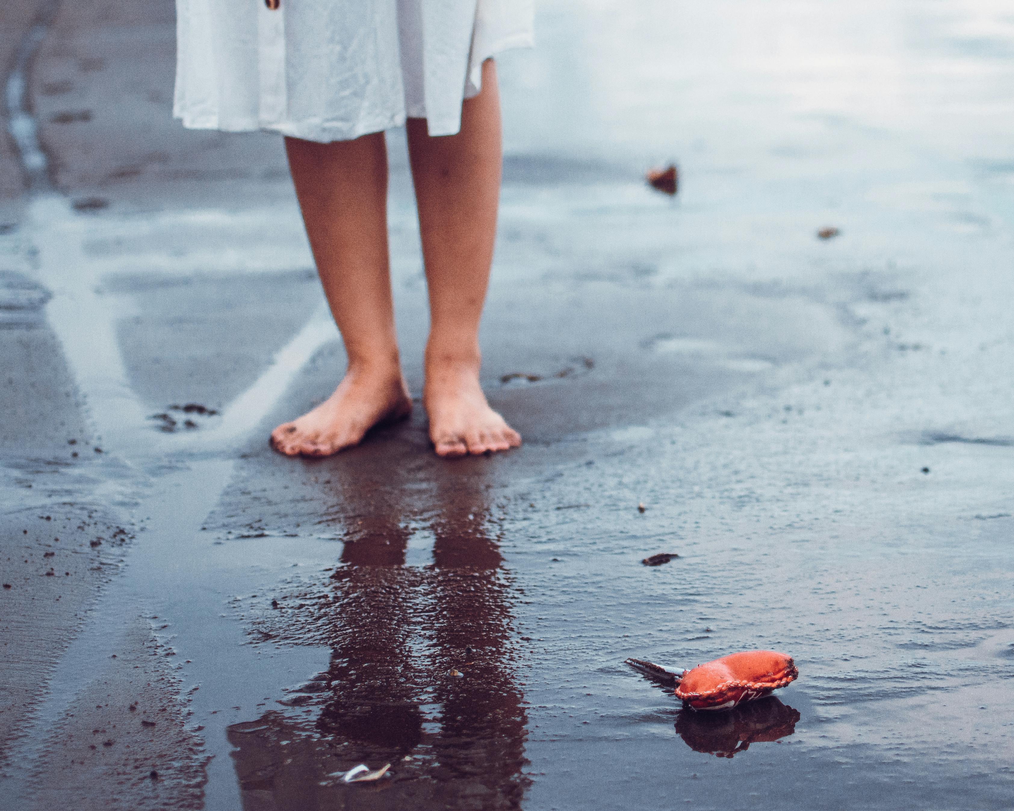 crop unrecognizable woman in dress standing on wet sandy beach